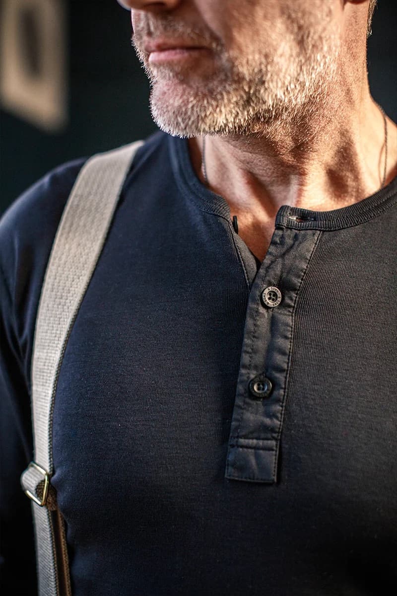 Close-up of a man wearing a dark navy henley shirt with a gray fabric shoulder strap crossing the chest.