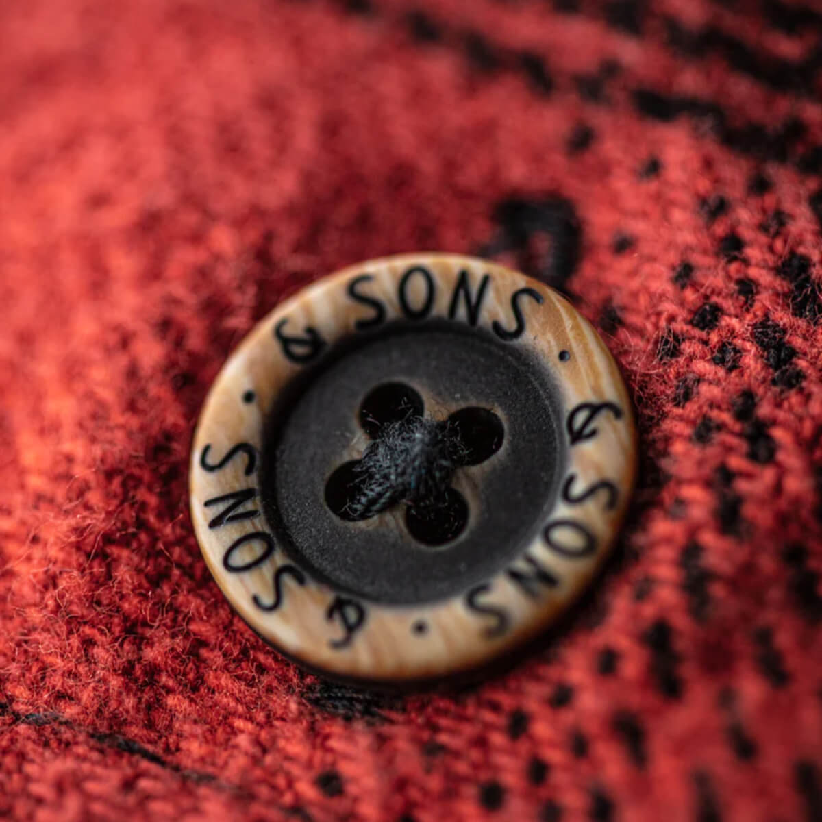 Close-up of a button with &SONS text on a red fabric background