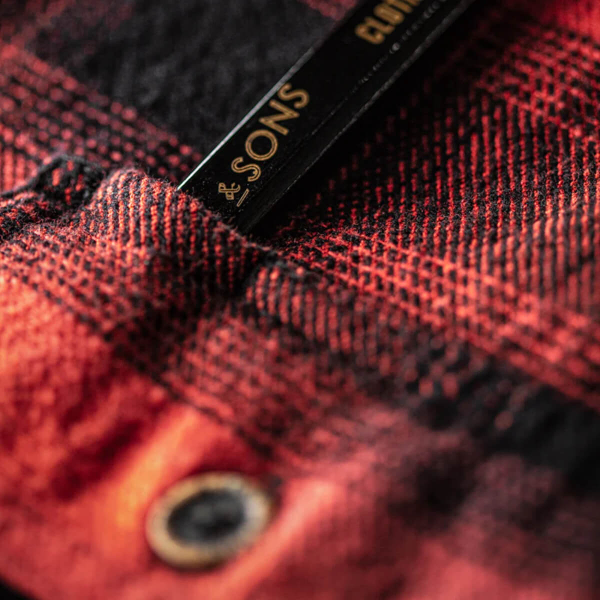 Close-up of a red and black checkered fabric with &Sons' branding.