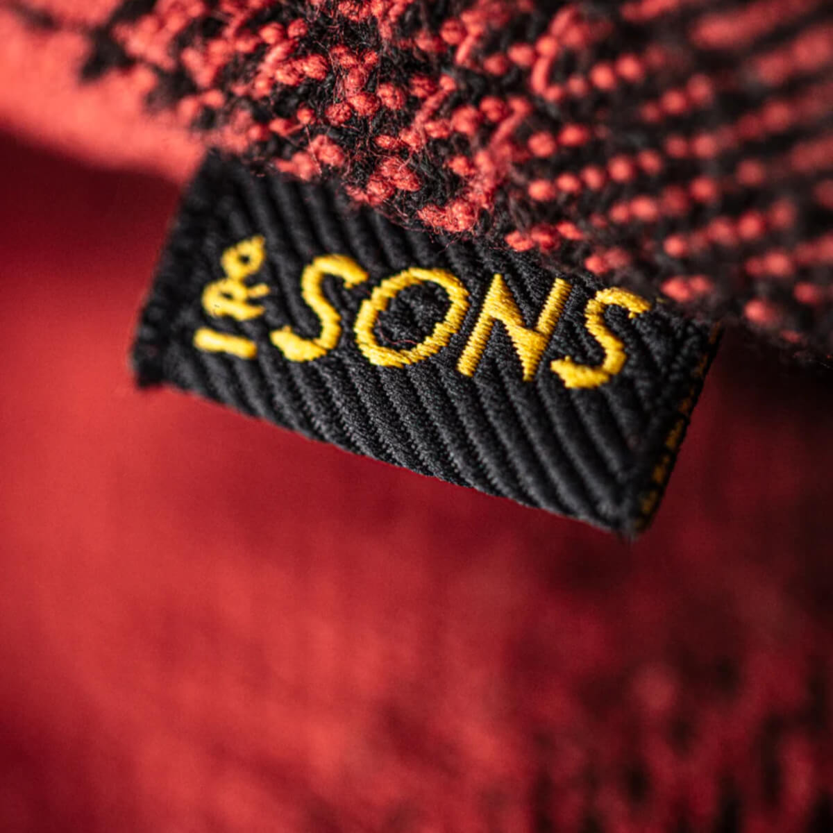 Close-up of a textured fabric with &Sons logo on a red background