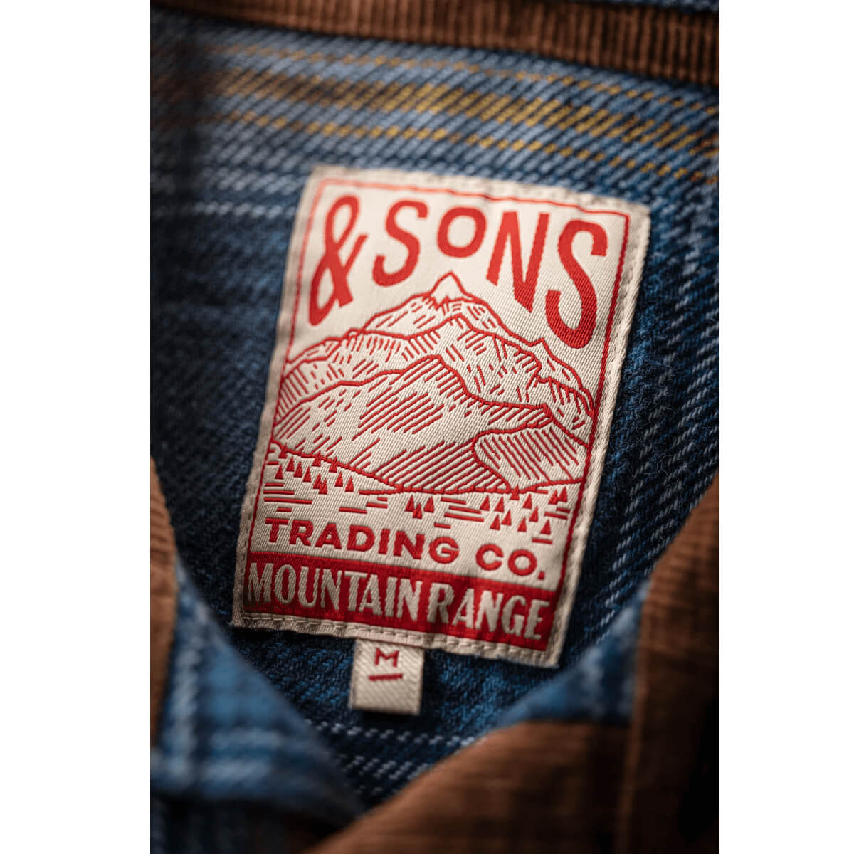 Close-up of a denim fabric with a 'and Sons Trading Co. Mountain Range' label.