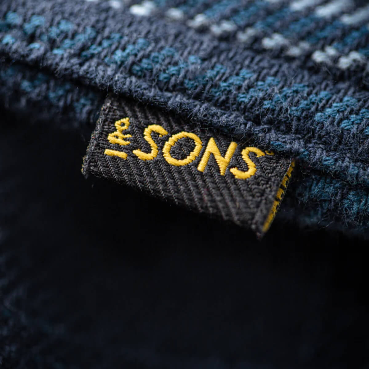 Close-up of a 'The Sons' label on denim fabric.