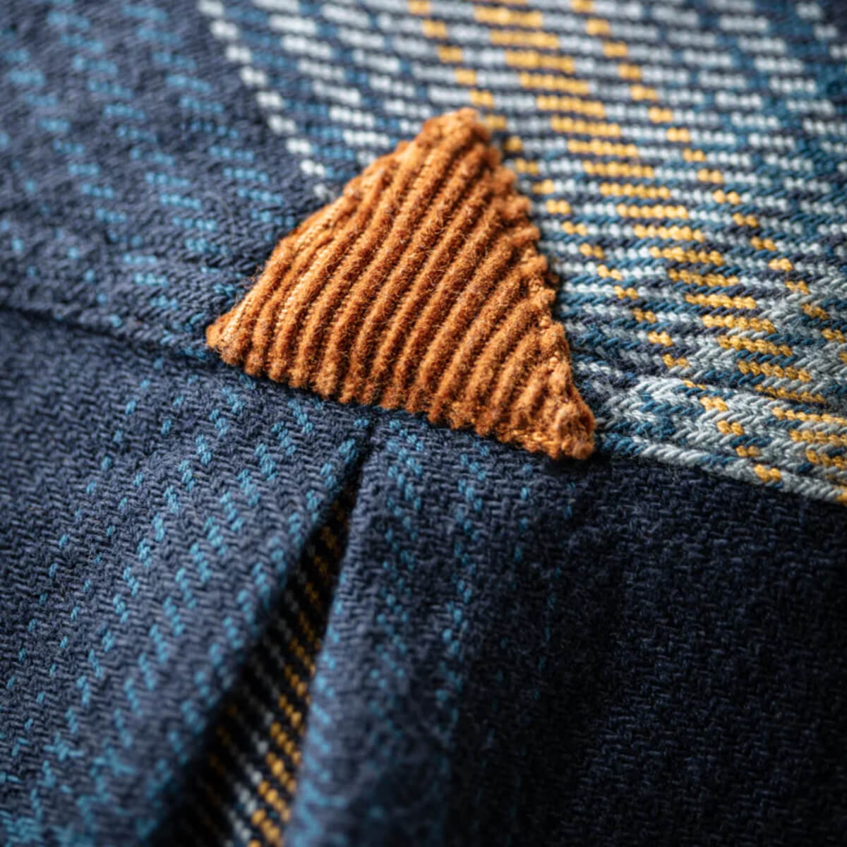Close-up of a textured brown patch on blue fabric with yellow accents
