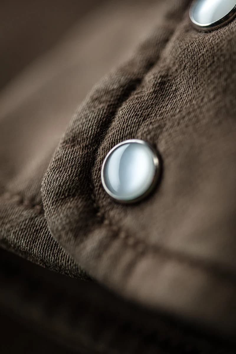 Close-up of a brown textured fabric garment with a silver metal snap button.