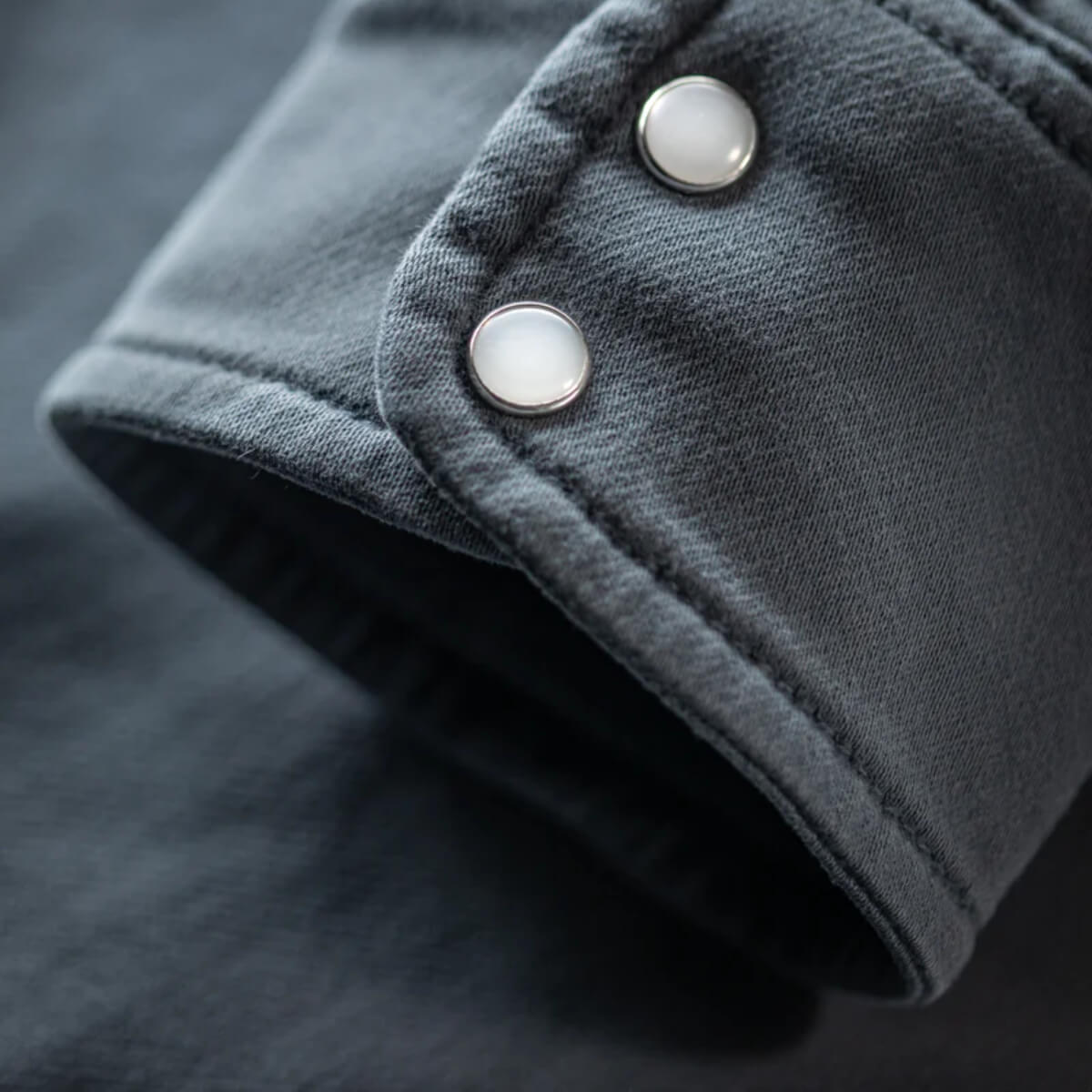 Close-up of a dark gray fabric with two silver buttons on a black background