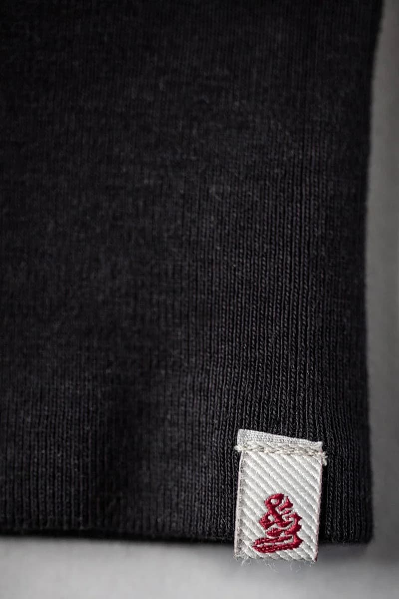 Close-up of a black ribbed knit garment cuff with a small white fabric tag featuring a red embroidered logo.