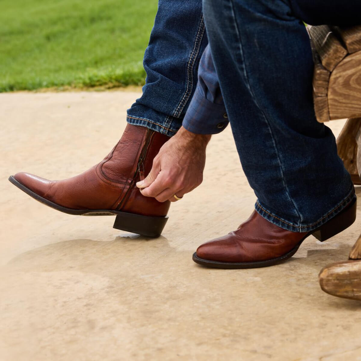 Person wearing brown leather cowboy boots and blue jeans sitting on a wooden stool.