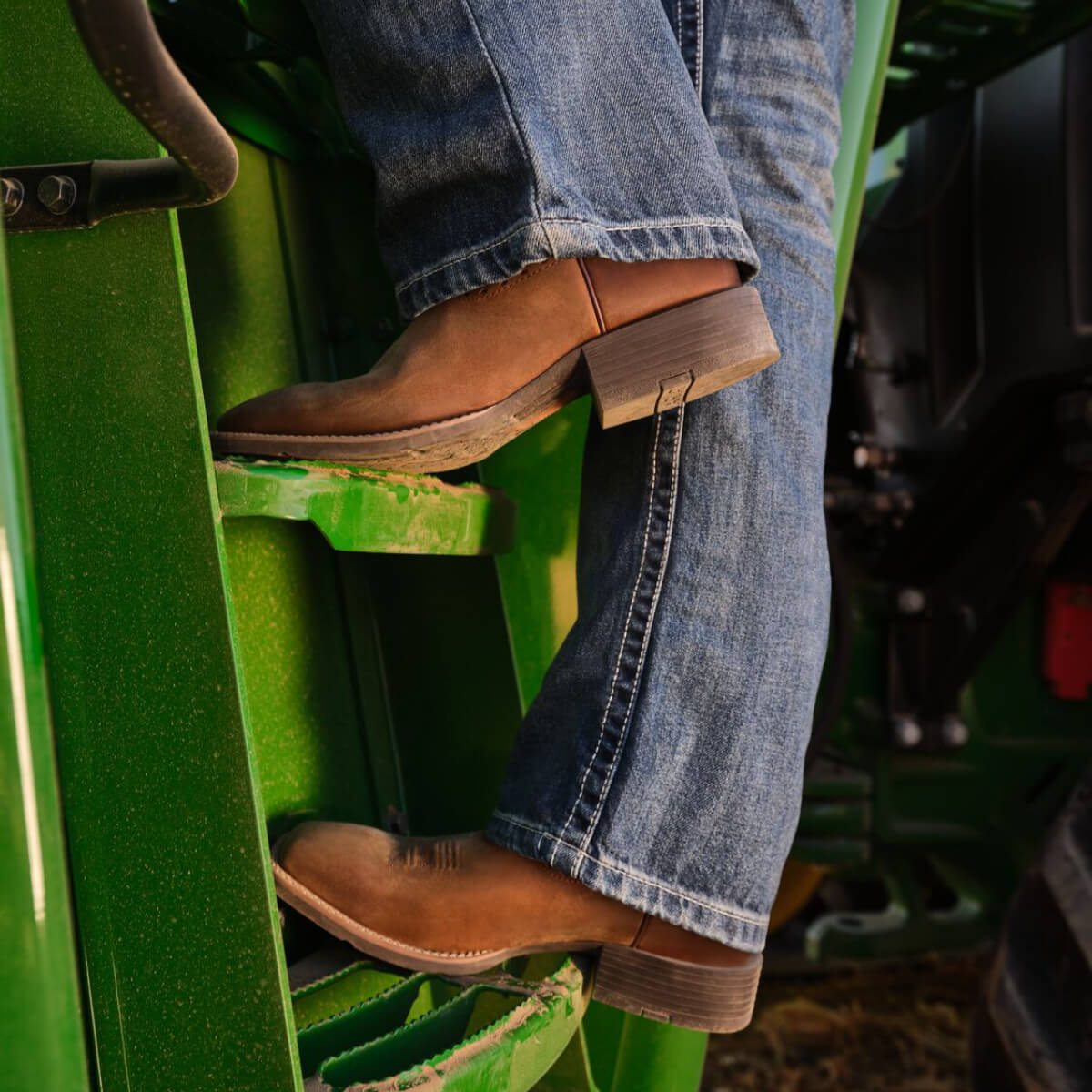 Person wearing brown boots and blue jeans climbing a green ladder.