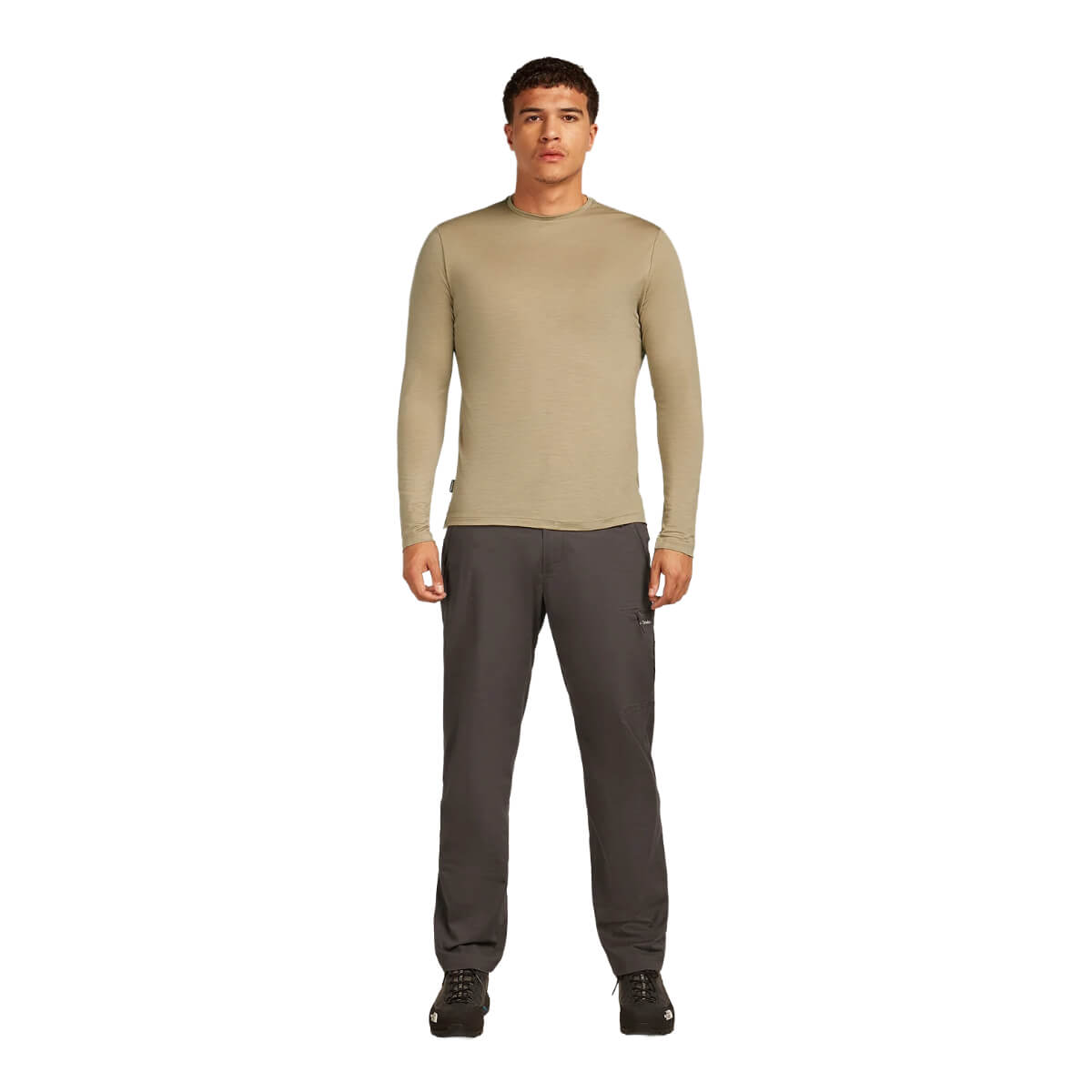 Man wearing a beige long-sleeve shirt and dark pants on a white background