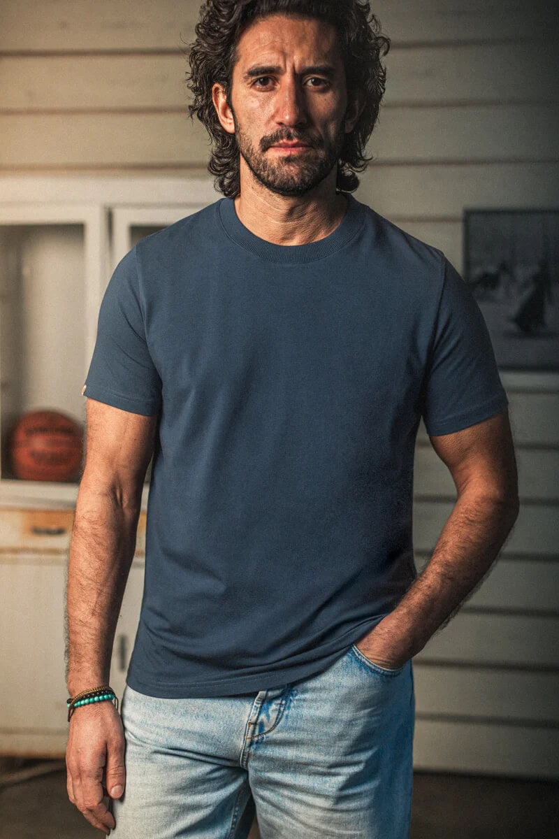 Man wearing a blue t-shirt and jeans standing indoors.