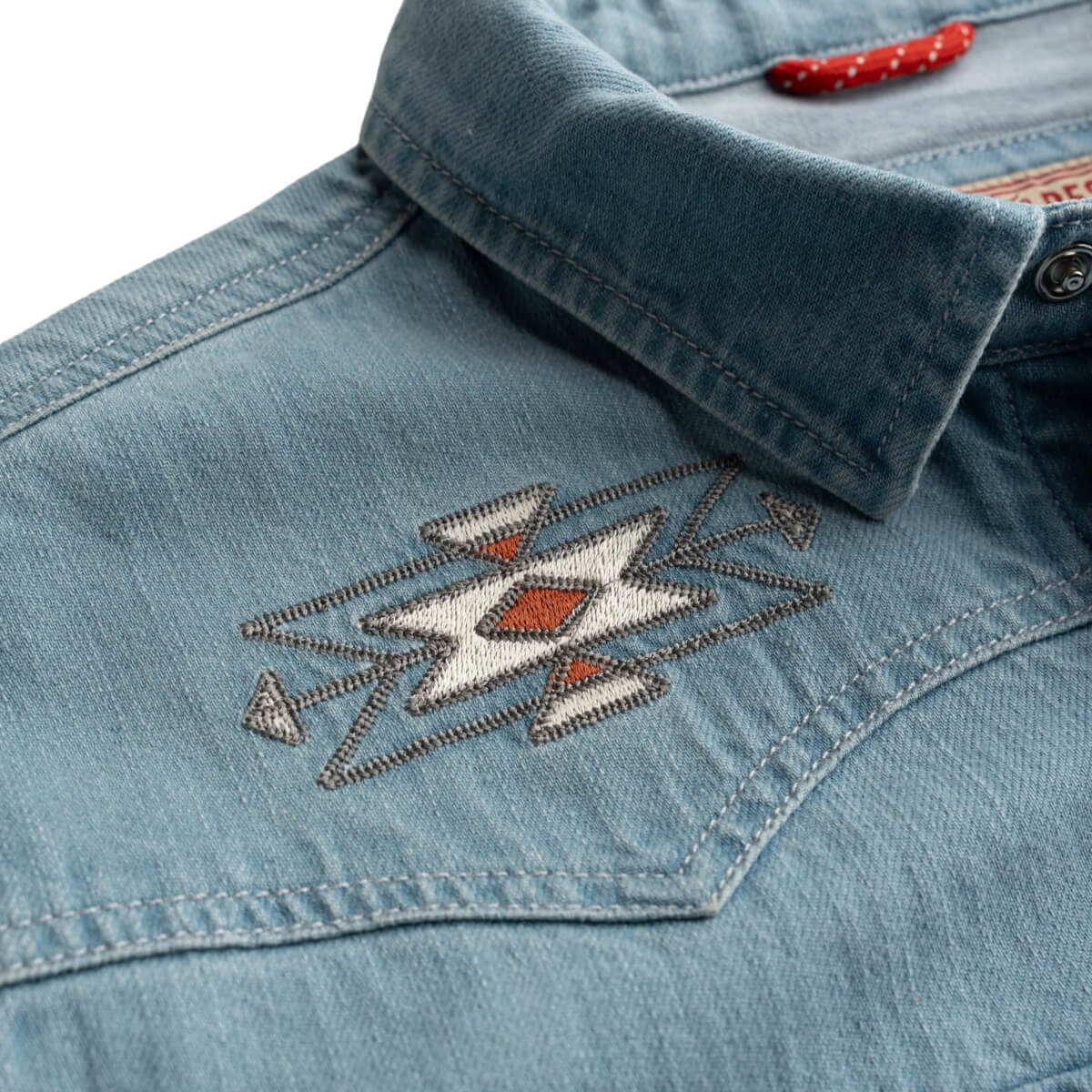 Close-up of a blue denim shirt with an embroidered design on the collar.