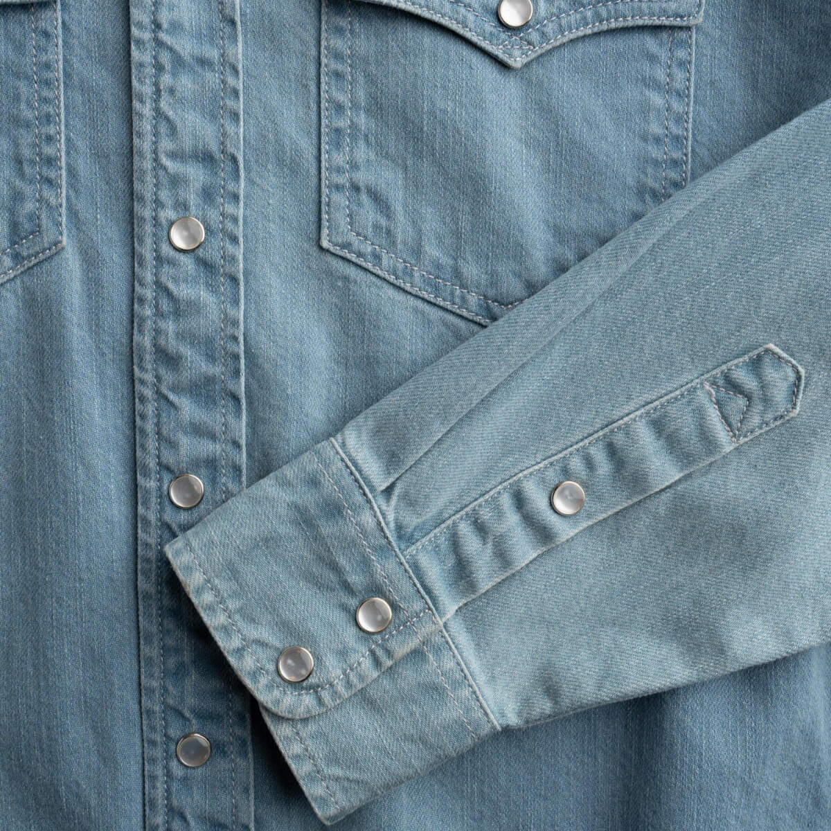 Close-up of a blue denim shirt with buttons and stitching details.