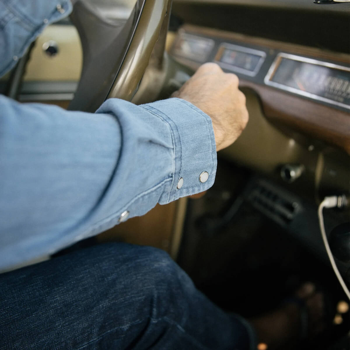 Person driving a car with a focus on the steering wheel and dashboard.
