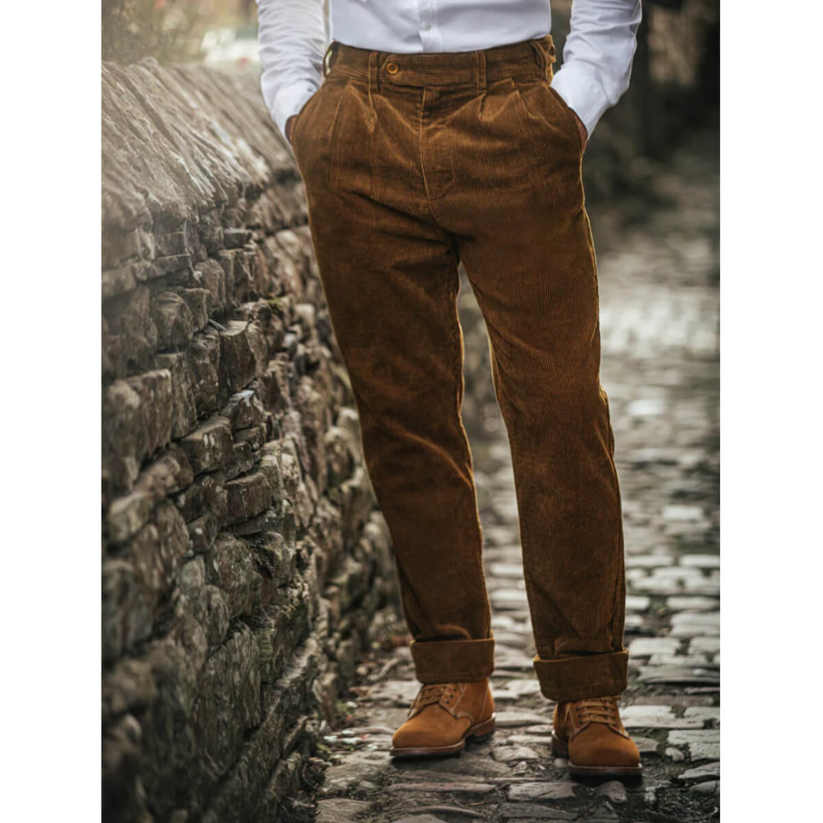 Person wearing brown corduroy pants and brown boots standing against a stone wall.