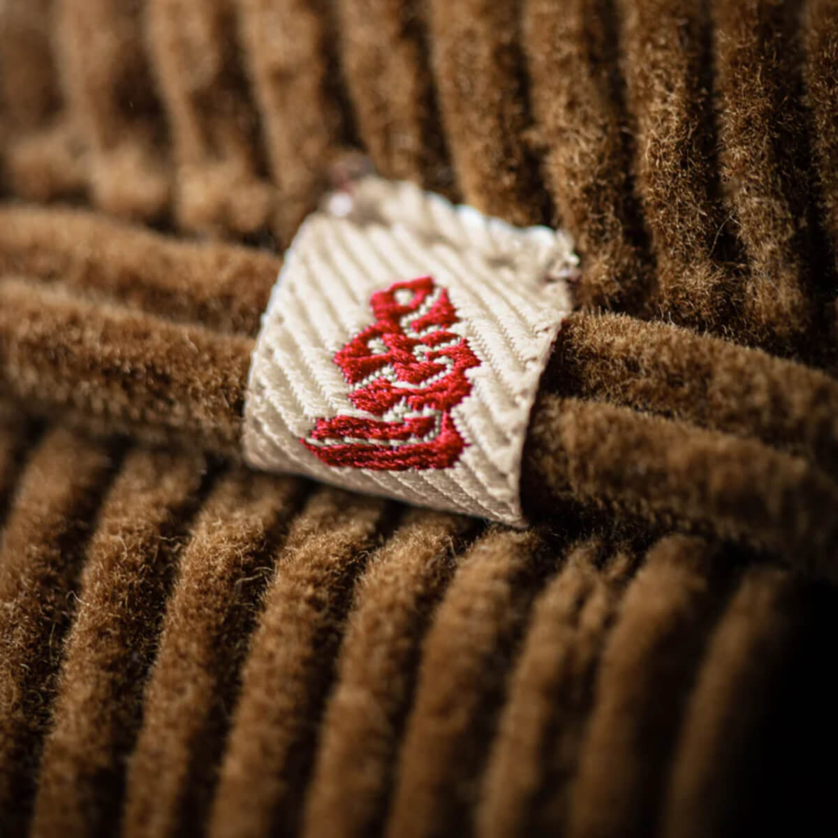 Close-up of a brown textured fabric with a white tag featuring red text.