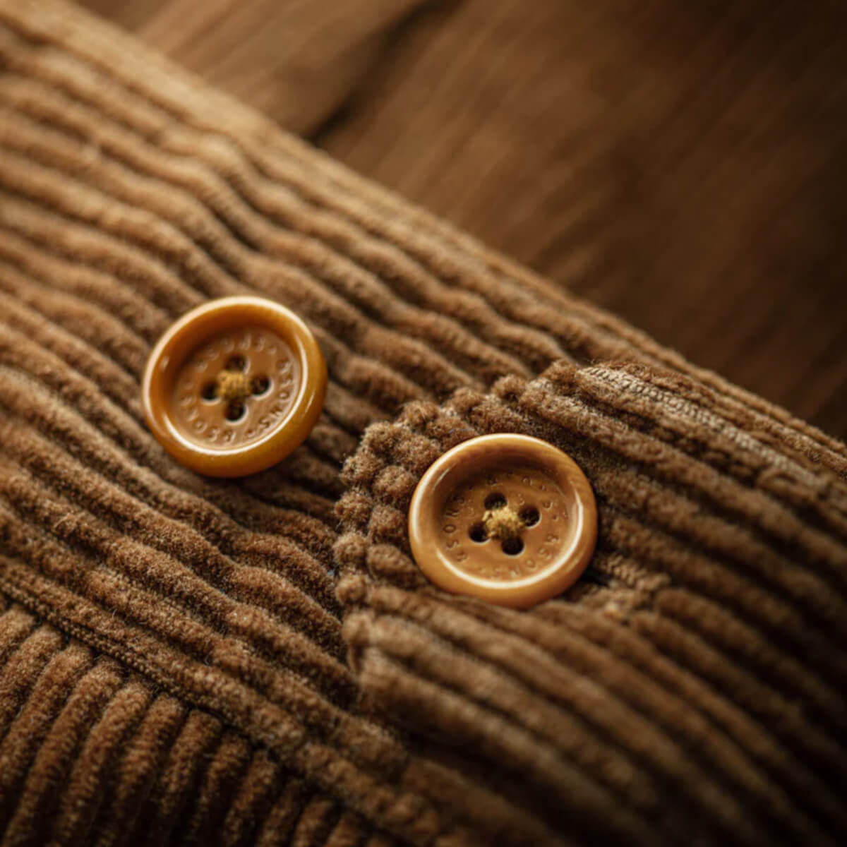 Close-up of brown corduroy fabric with two buttons on a wooden surface