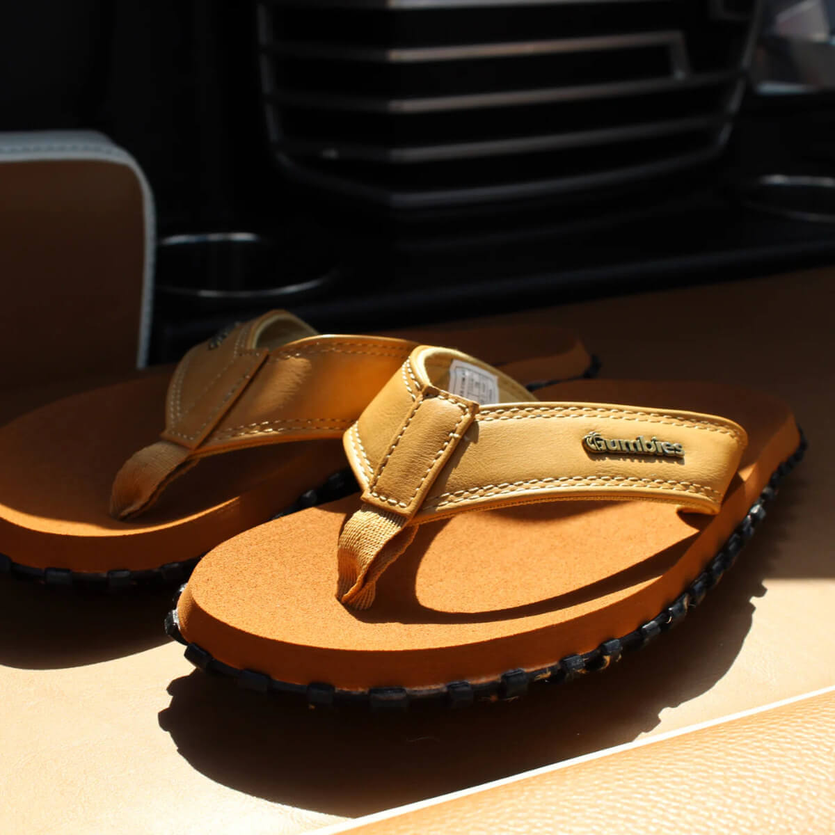 Pair of tan sandals on a vehicle seat with &#39;Gumbies&#39; branding.