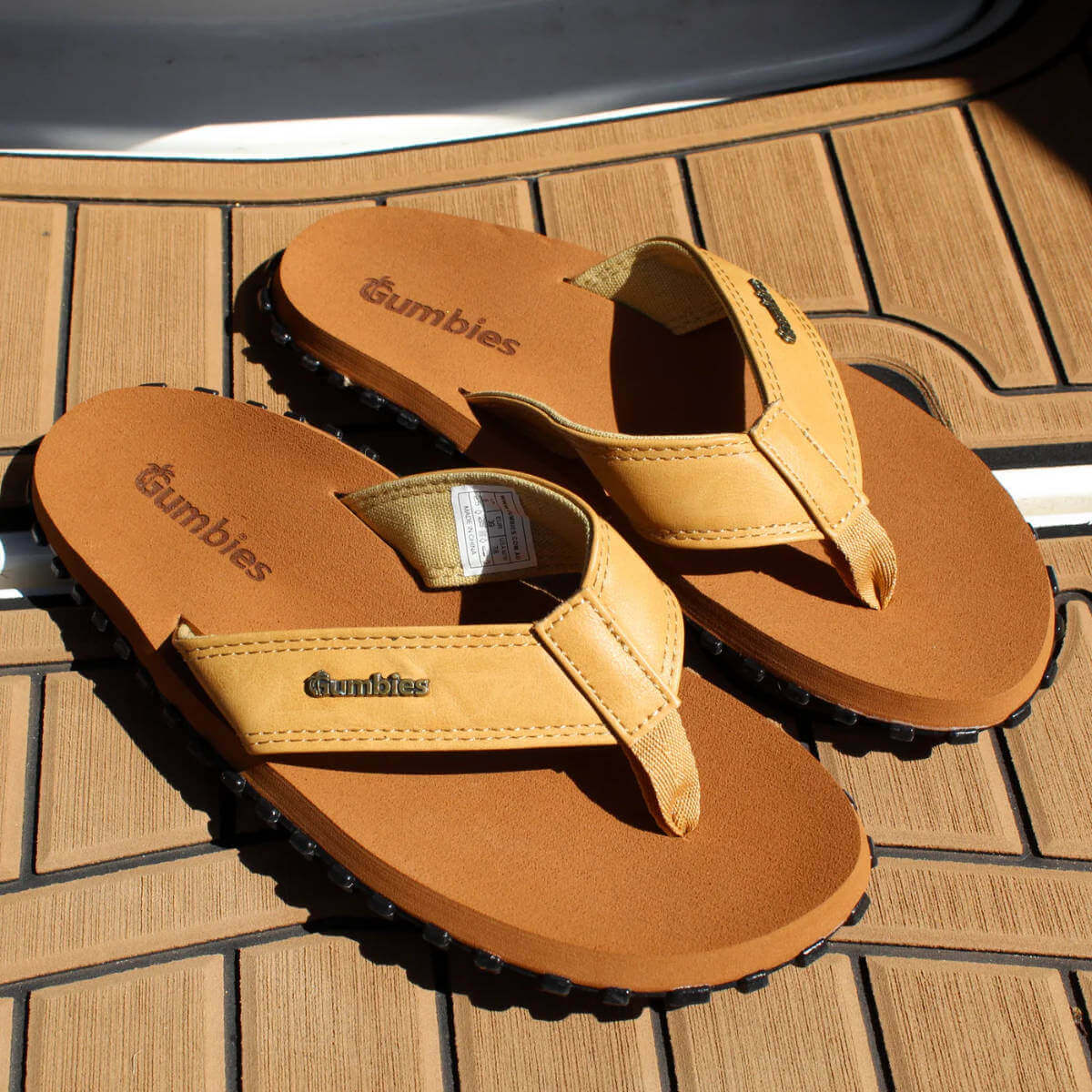 Pair of tan sandals with Gumbies branding on a wooden deck.